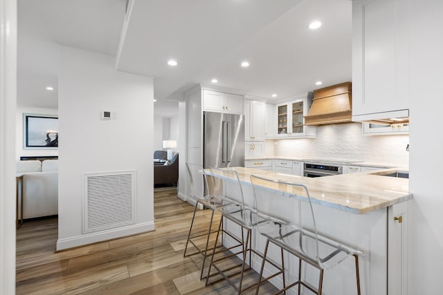 1131 Stringers Ridge Rd Unit 12E, Chattanooga, TN 37405 - kitchen featuring custom range hood, a peninsula, light stone counters, light wood finished floors, and white cabinets