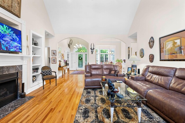 902 Cattails Dr, Ooltewah, TN 37363 - living room featuring arched walkways, a chandelier, built in shelves, high vaulted ceiling, and a premium fireplace