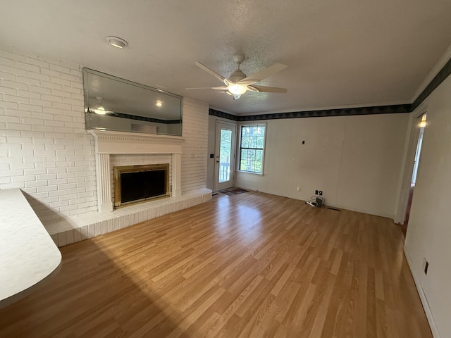 30551 Al Al Unit 71, Bryant, AL 35958 - unfurnished living room featuring a ceiling fan, wood finished floors, a brick fireplace, crown molding, and a textured ceiling