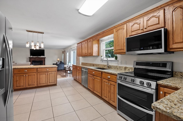 7470 Jester Ct, Ooltewah, TN 37363 - kitchen with stainless steel appliances, a fireplace, hanging light fixtures, light tile patterned floors, and light stone counters