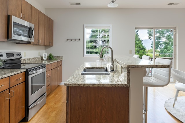 844 E 8th St, Chattanooga, TN 37403 - kitchen with stainless steel appliances, a kitchen bar, light wood-style flooring, an island with sink, and brown cabinetry