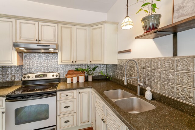 4503 Saint Elmo Ave, Chattanooga, TN 37409 - kitchen featuring stainless steel electric stove, cream cabinetry, under cabinet range hood, backsplash, and decorative light fixtures