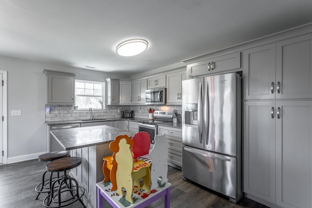 9600 Lovell Rd, Soddy Daisy, TN 37379 - kitchen with stainless steel appliances, gray cabinets, a breakfast bar area, decorative backsplash, and dark wood-style flooring