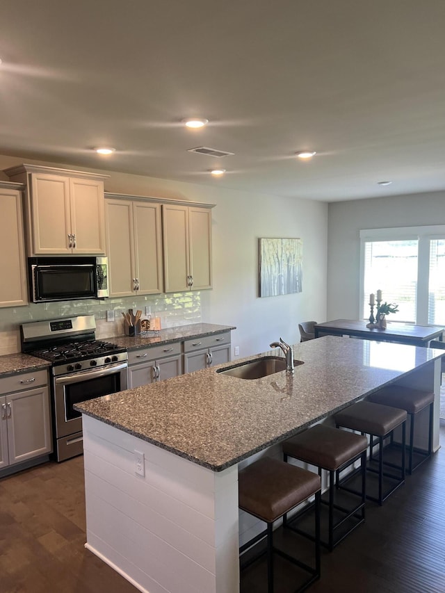 3309 Grassy Fields Ln, Apison, TN 37302 - kitchen with gas stove, a breakfast bar, a kitchen island with sink, dark stone counters, and decorative backsplash