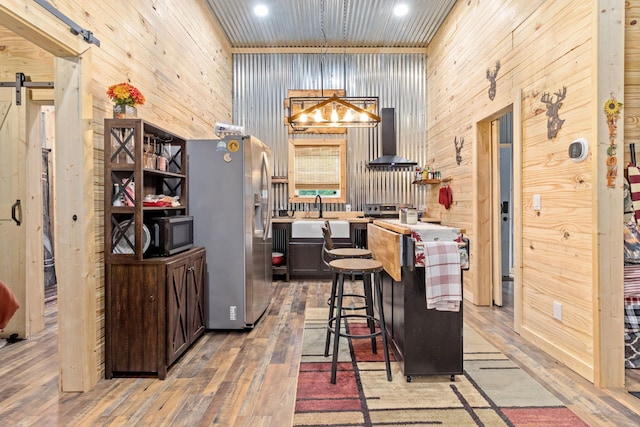 1780 Wolf Haven Rd, Spencer, TN 38585 - kitchen featuring stainless steel refrigerator with ice dispenser, a barn door, wall chimney exhaust hood, light wood-style flooring, and wooden walls