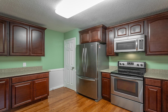8217 Rolling Stone Ln, Ooltewah, TN 37363 - kitchen with stainless steel appliances, light wood-type flooring, a textured ceiling, a wainscoted wall, and light countertops