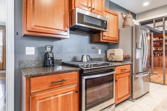 7918 Chianti Way, Chattanooga, TN 37421 - kitchen featuring appliances with stainless steel finishes, light tile patterned floors, dark stone counters, and brown cabinets