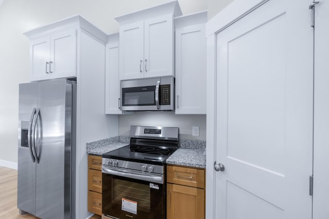 307 Cavender St, Lafayette, GA 30728 - kitchen with appliances with stainless steel finishes, light stone countertops, white cabinets, and light wood-type flooring
