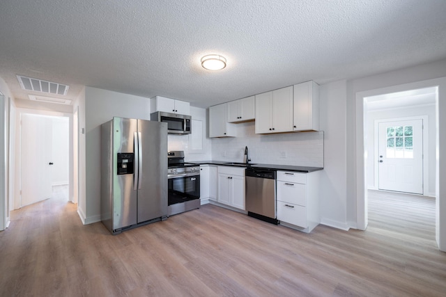 103 Laurel Dr, Chattanooga, TN 37415 - kitchen with stainless steel appliances, dark countertops, light wood-style flooring, white cabinetry, and tasteful backsplash