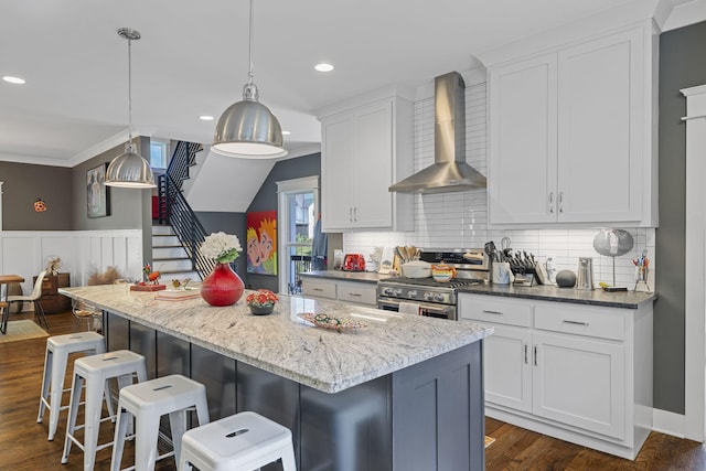 834 Dartmouth St, Chattanooga, TN 37405 - kitchen featuring wall chimney range hood, stainless steel range with gas stovetop, white cabinets, a kitchen island, and a kitchen bar