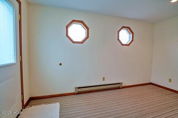 carpeted empty room featuring a baseboard heating unit