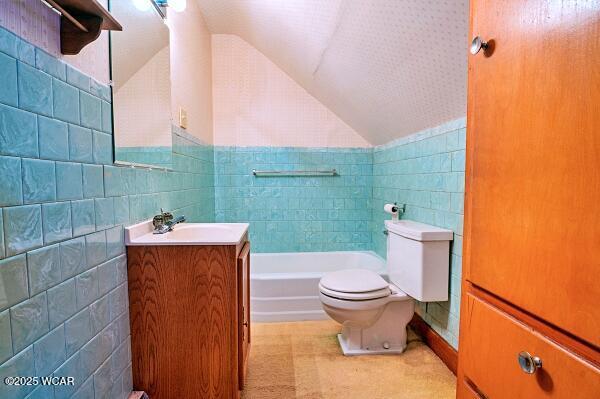 bathroom featuring lofted ceiling, tile walls, a bathtub, vanity, and toilet