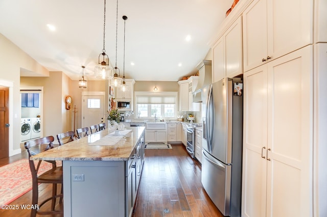 kitchen featuring a center island, hanging light fixtures, appliances with stainless steel finishes, a kitchen breakfast bar, and light stone countertops