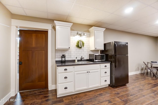 kitchen featuring sink, black refrigerator, white cabinetry, tasteful backsplash, and dark hardwood / wood-style flooring