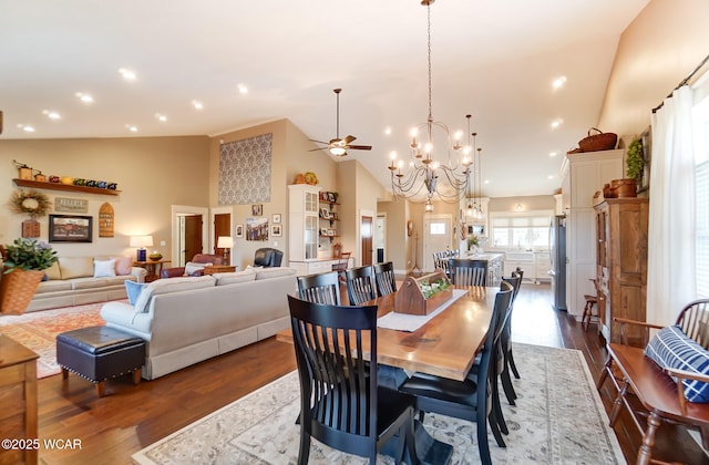 dining room with ceiling fan with notable chandelier, dark hardwood / wood-style floors, and high vaulted ceiling