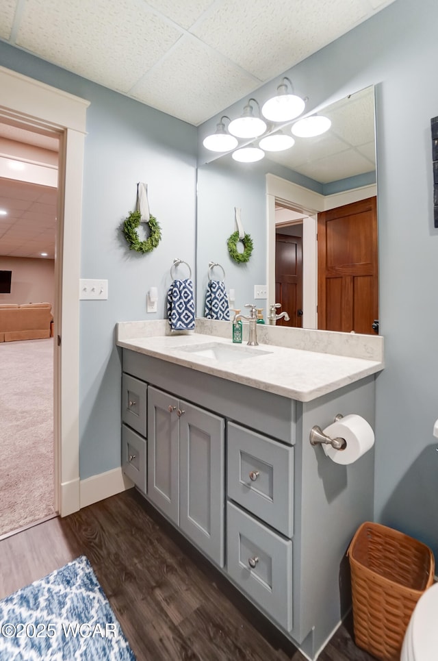 bathroom featuring wood-type flooring, a drop ceiling, and vanity