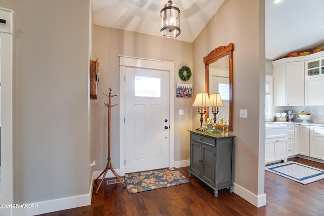 foyer entrance featuring lofted ceiling, dark wood-type flooring, and a chandelier