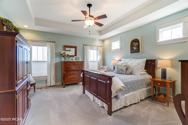 carpeted bedroom with a raised ceiling, ceiling fan, and multiple windows