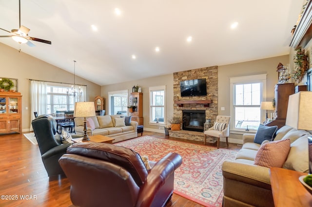 living room featuring lofted ceiling, hardwood / wood-style flooring, a stone fireplace, and ceiling fan with notable chandelier