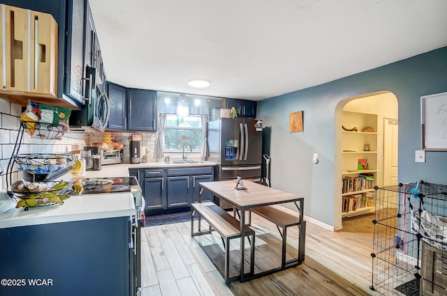 kitchen featuring sink, appliances with stainless steel finishes, backsplash, light hardwood / wood-style floors, and blue cabinets