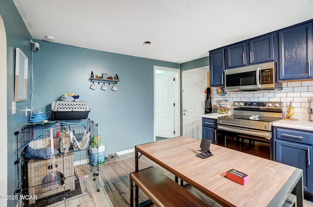 kitchen featuring stainless steel appliances, tasteful backsplash, wood-type flooring, and blue cabinets