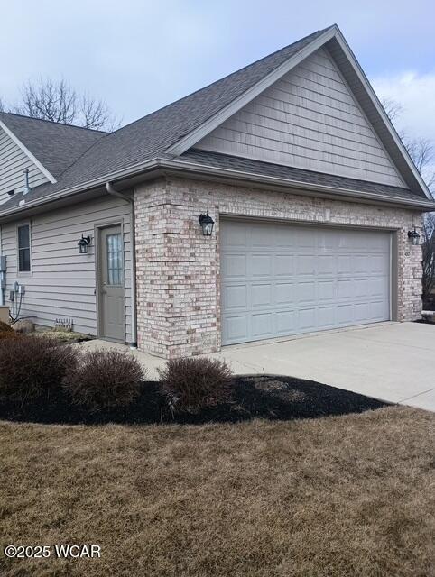 view of front of home featuring a front lawn, roof with shingles, concrete driveway, a garage, and brick siding