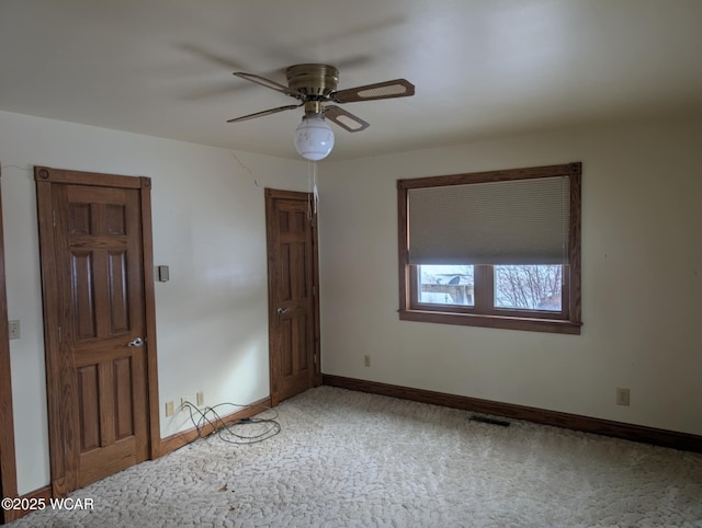 empty room with a ceiling fan, light colored carpet, visible vents, and baseboards