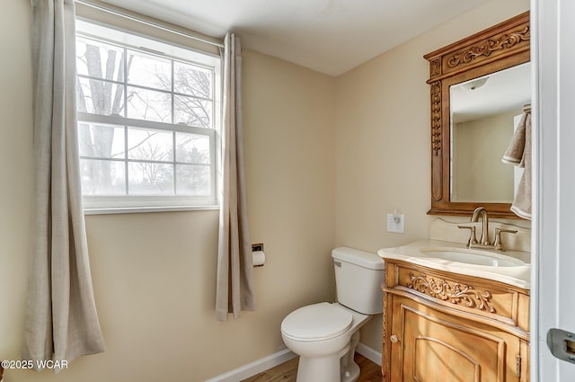 half bathroom with baseboards, toilet, and vanity