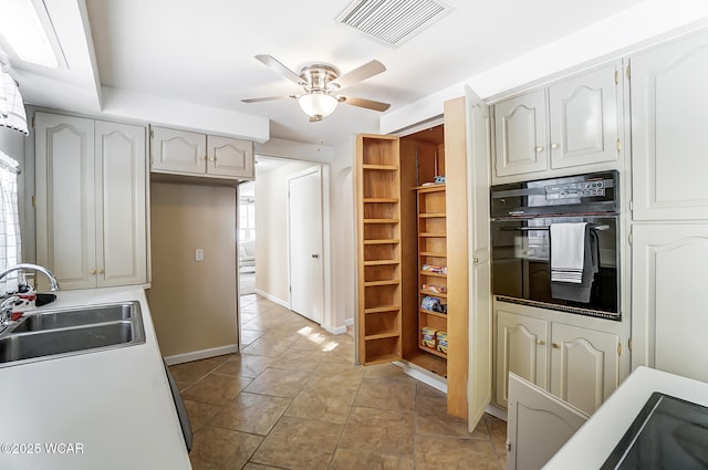 kitchen with light tile patterned floors, a ceiling fan, visible vents, a sink, and black oven