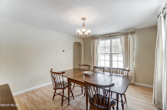 dining space featuring baseboards, arched walkways, a notable chandelier, and light wood-style flooring