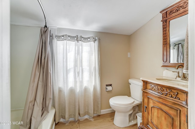 bathroom with baseboards, toilet, shower / tub combo with curtain, wood finished floors, and vanity