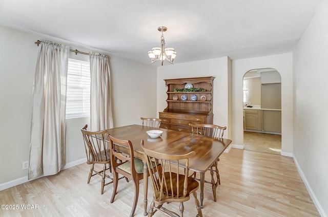 dining space featuring an inviting chandelier, light wood-style flooring, baseboards, and arched walkways