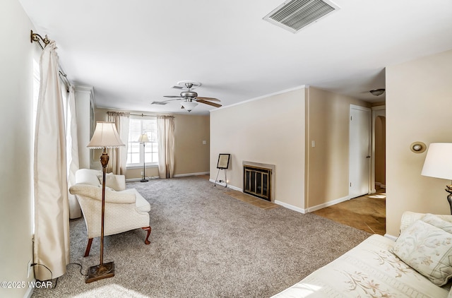 carpeted living room featuring visible vents, baseboards, a glass covered fireplace, and a ceiling fan