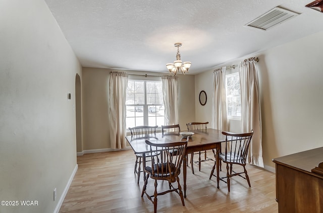 dining room featuring visible vents, arched walkways, light wood-style floors, and an inviting chandelier