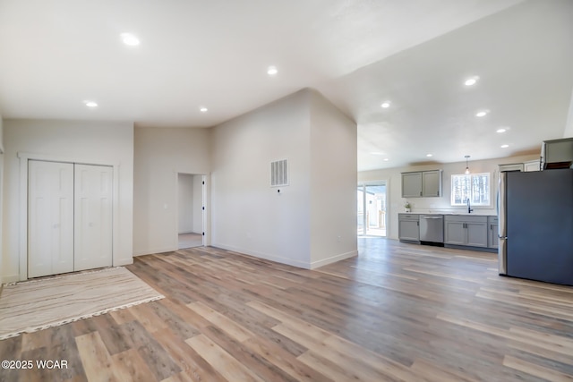 unfurnished living room with visible vents, light wood finished floors, baseboards, recessed lighting, and lofted ceiling