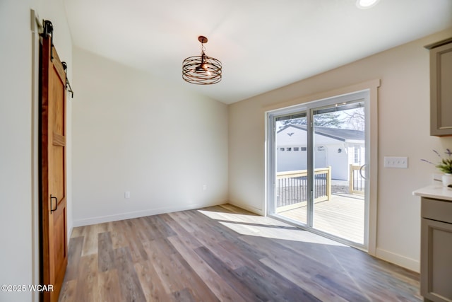 unfurnished dining area featuring a notable chandelier, baseboards, a barn door, and light wood-type flooring