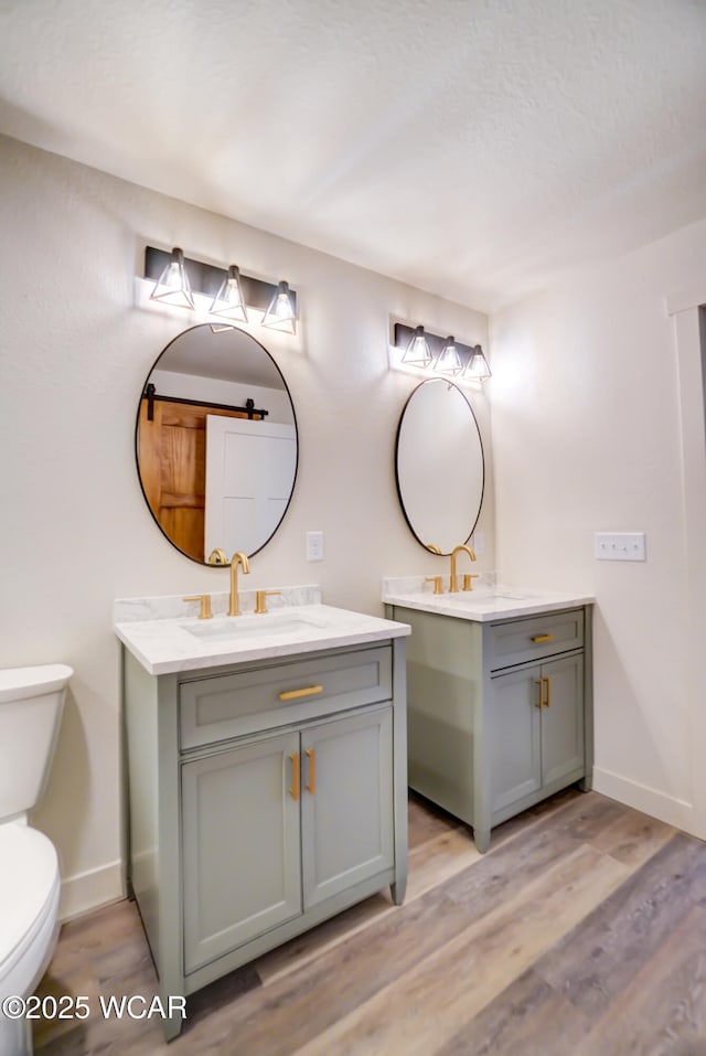 bathroom featuring baseboards, toilet, wood finished floors, two vanities, and a sink
