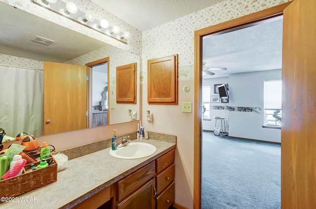 bathroom with a textured ceiling, visible vents, baseboards, ceiling fan, and wallpapered walls
