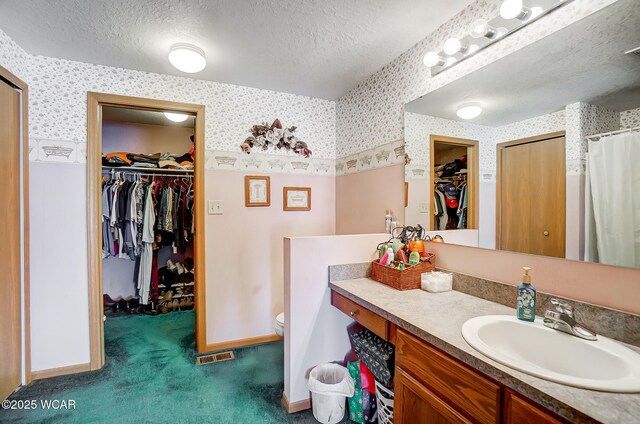 full bath with baseboards, a textured ceiling, wallpapered walls, and vanity
