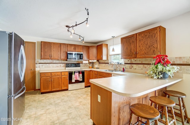 kitchen with light countertops, brown cabinetry, a peninsula, and appliances with stainless steel finishes