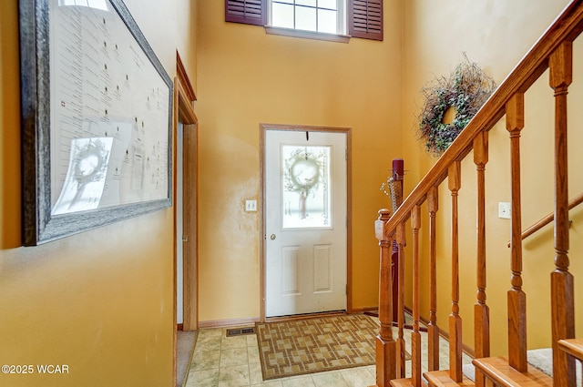 foyer entrance featuring a high ceiling, baseboards, stairway, and visible vents