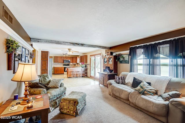 living area featuring light carpet, a textured ceiling, visible vents, beamed ceiling, and ceiling fan