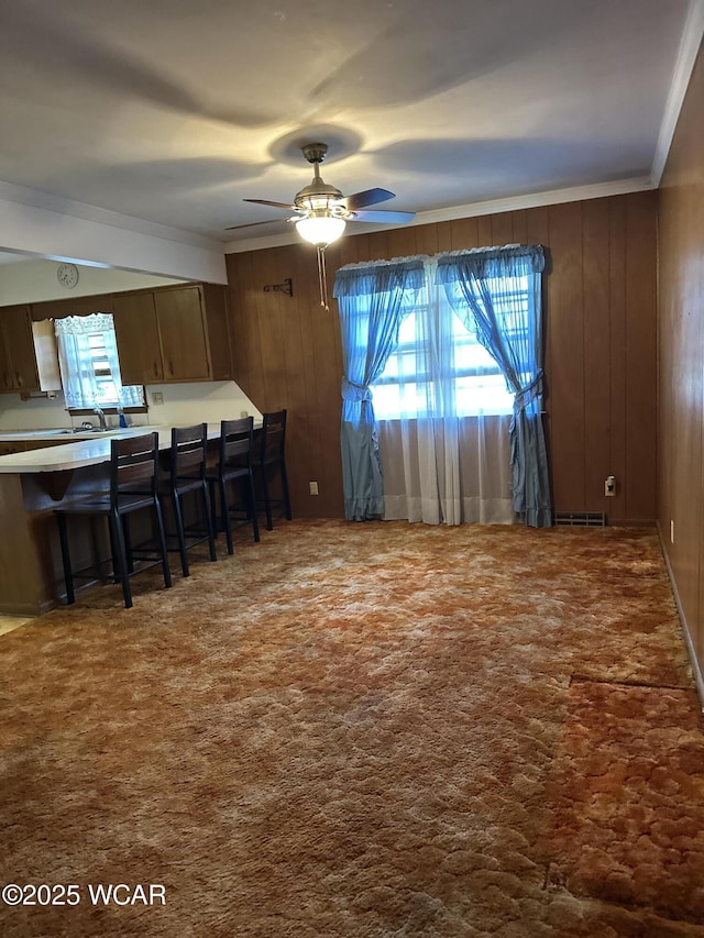1115 Fett Ave, Lima, OH 45801 - kitchen featuring ornamental molding, ceiling fan, a breakfast bar, wooden walls, and carpet flooring