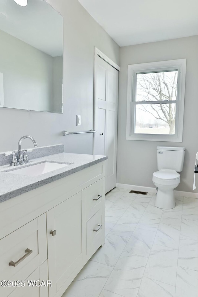bathroom with toilet, vanity, marble finish floor, baseboards, and visible vents