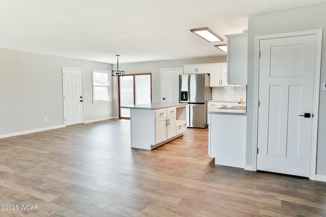 kitchen with white cabinetry, a center island, light wood-type flooring, stainless steel refrigerator with ice dispenser, and decorative backsplash