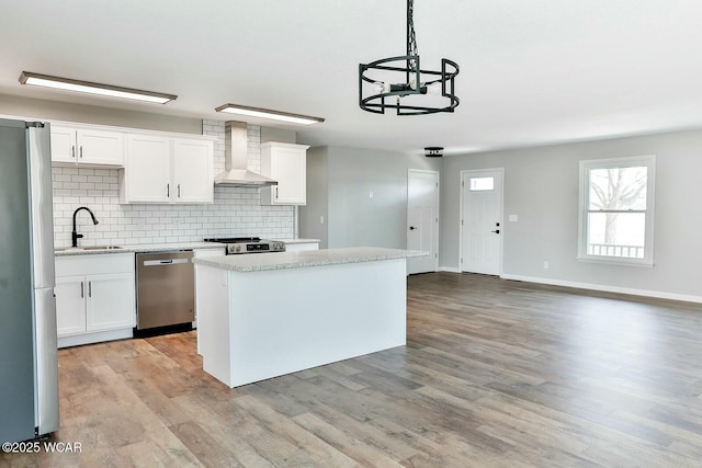 kitchen featuring tasteful backsplash, stainless steel appliances, a kitchen island, a sink, and wall chimney range hood
