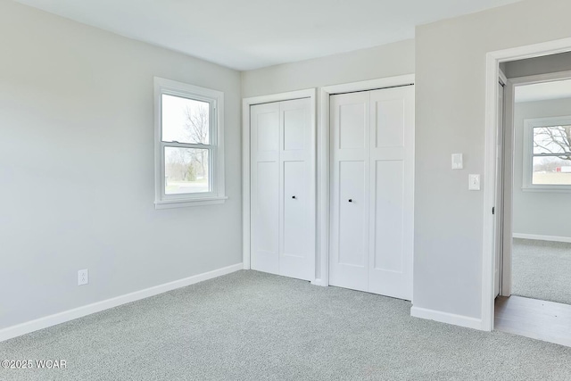 unfurnished bedroom with two closets, carpet floors, and baseboards