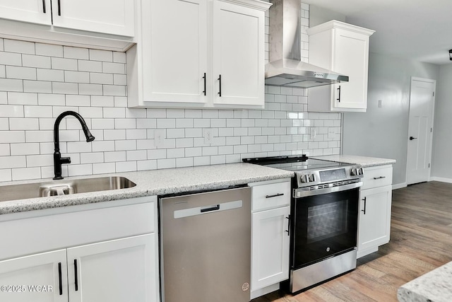 kitchen featuring a sink, light wood-type flooring, stainless steel appliances, wall chimney range hood, and white cabinets