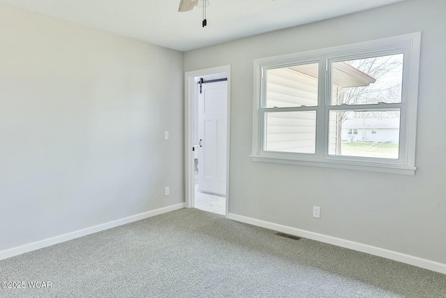 carpeted empty room featuring plenty of natural light, baseboards, visible vents, and a ceiling fan