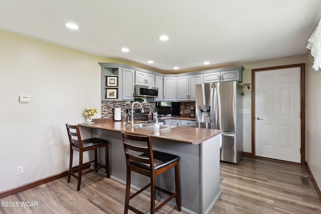 2855 State Route 67, Belle Center, OH 43310 - kitchen with appliances with stainless steel finishes, a peninsula, a kitchen breakfast bar, backsplash, and light wood-type flooring